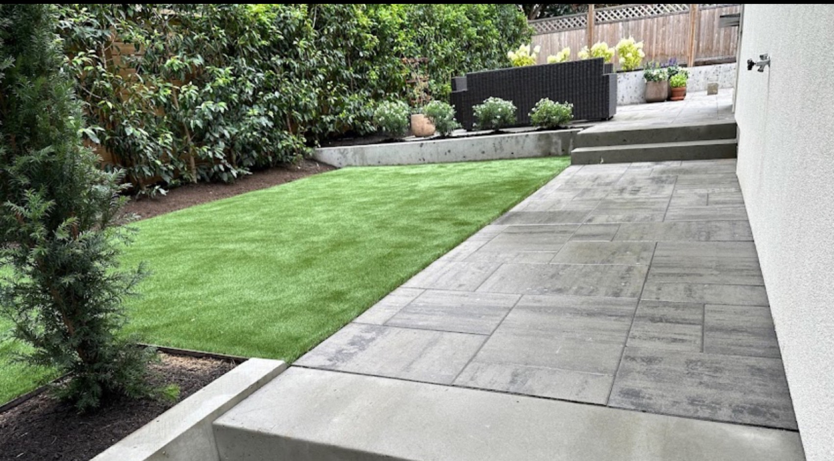 Artificial turf beside large format paving with planting and a rendered garden wall